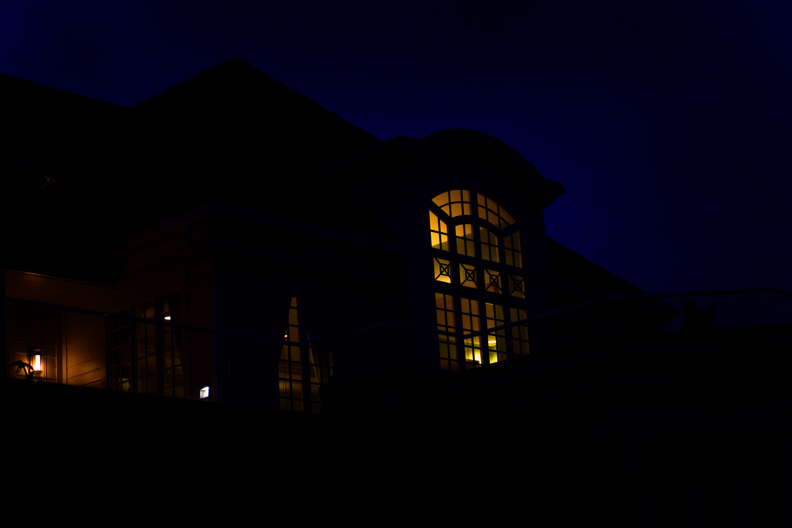 An under exposed building with a large lit up window.